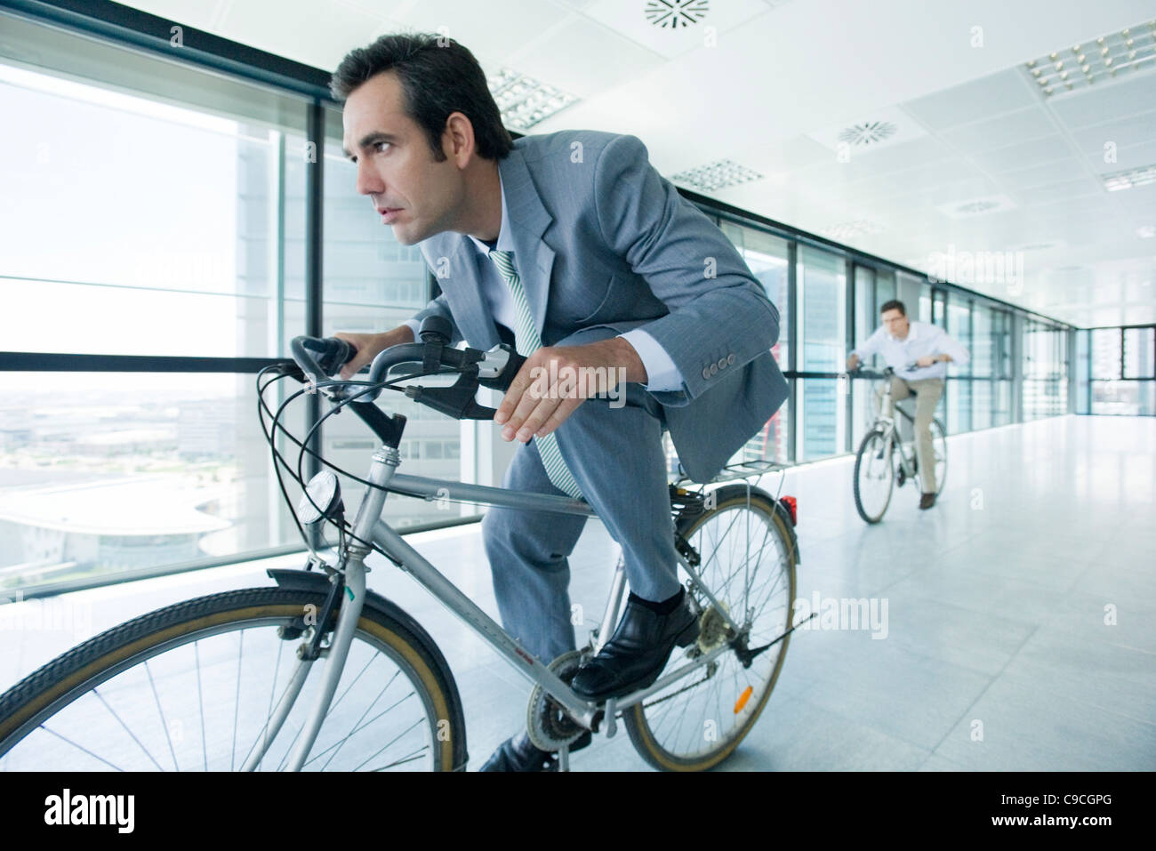 Businessmen riding bicycles indoors Stock Photo