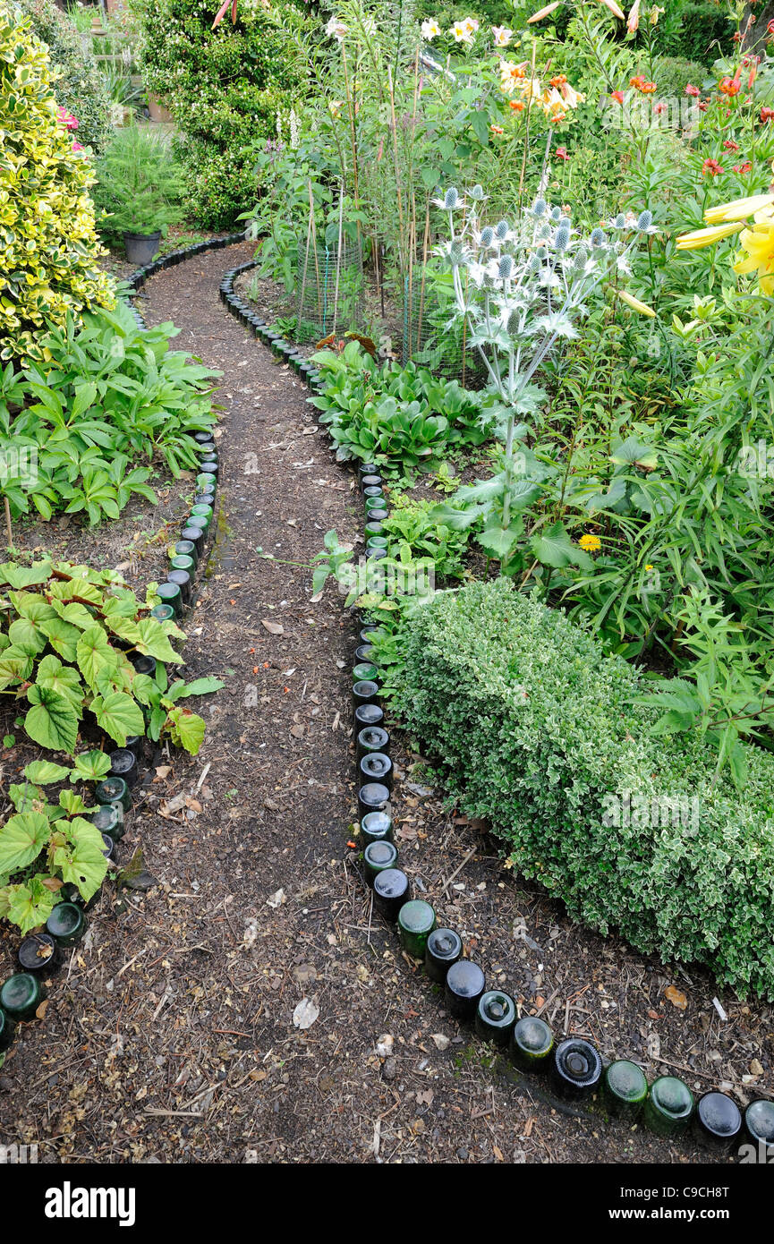 Bottle lined garden path leading through planted border of shrubs and flowers, Norfolk, England, July Stock Photo