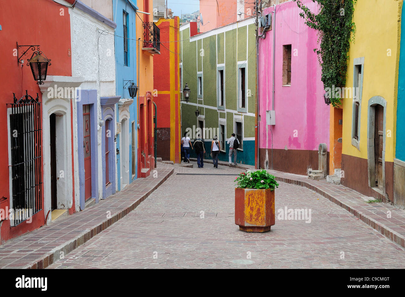Mexico, Bajio, Guanajuato, Paved street lined by colourfully painted houses, group of four people walking at far end and Stock Photo
