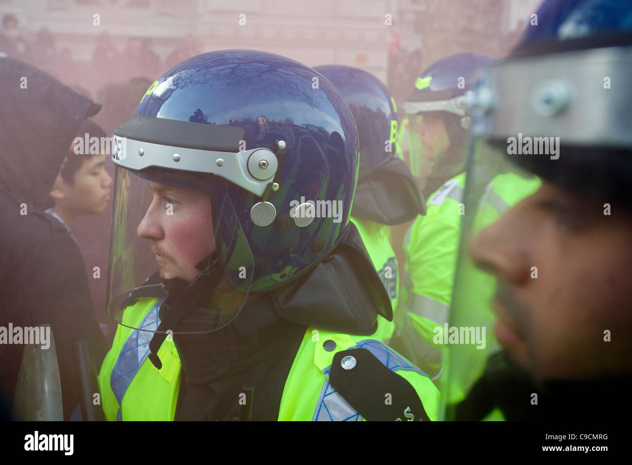 Police in riot gear forming a barrier on Whitehall, bathed in red smoke from a flare, Student Demonstration, London, England Stock Photo