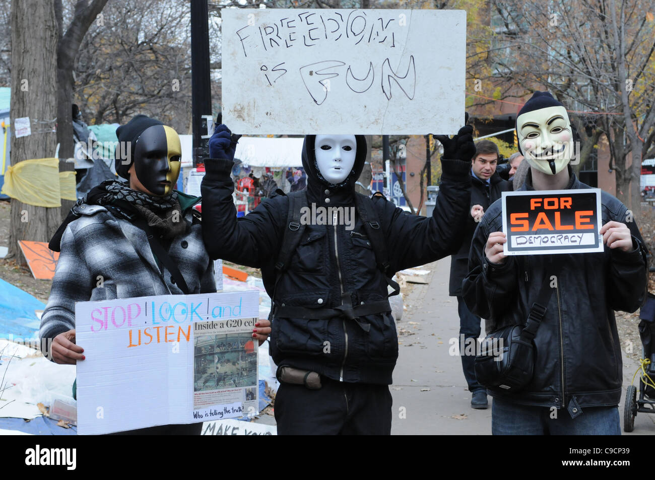 November 21, 2011, three masked protesters carry signs at St. James park following the decision handed down this morning by Ontario Superior Court judge David Brown, upholding the Occupy Toronto tent camp eviction. Stock Photo