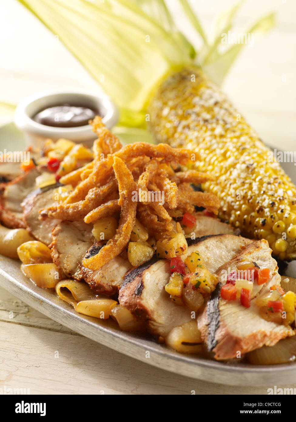 Chicken fajitas over vegetables topped with salsa and onion rings with an ear of grilled corn Stock Photo