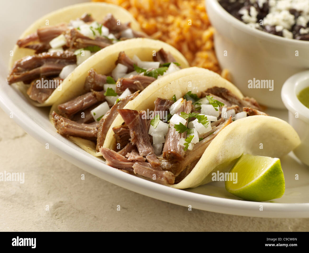Three carnitas street tacos topped with onion and cilantro served with black beans and Spanish rice Stock Photo