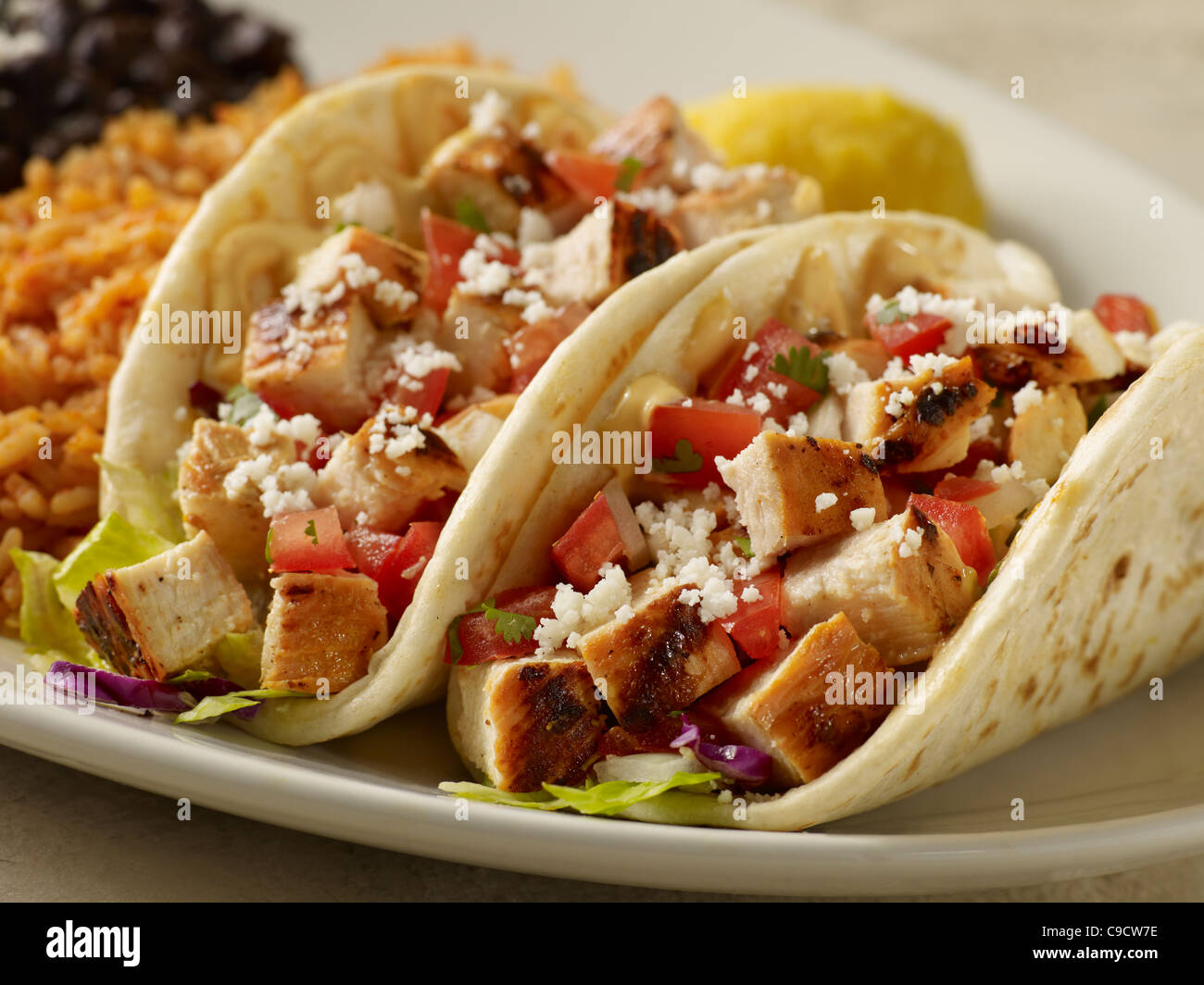 Two grilled chicken tacos topped with salsa and cheese served with black beans and Spanish rice Stock Photo