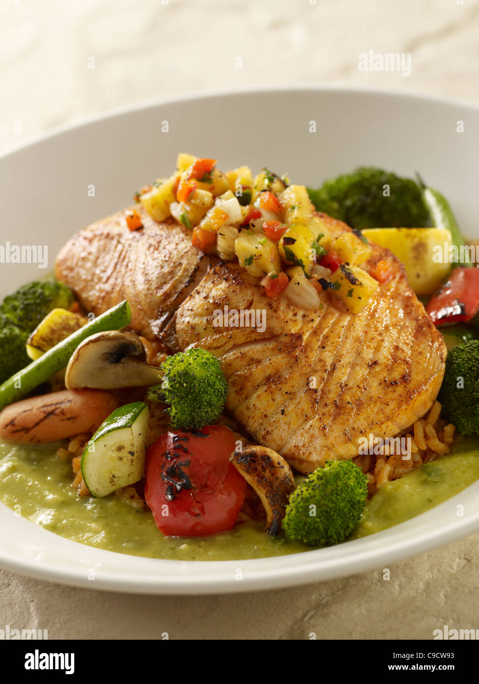 Grilled salmon fillet with a pineapple salsa served over vegetable and rice on a bed of green tomatillo sauce Stock Photo