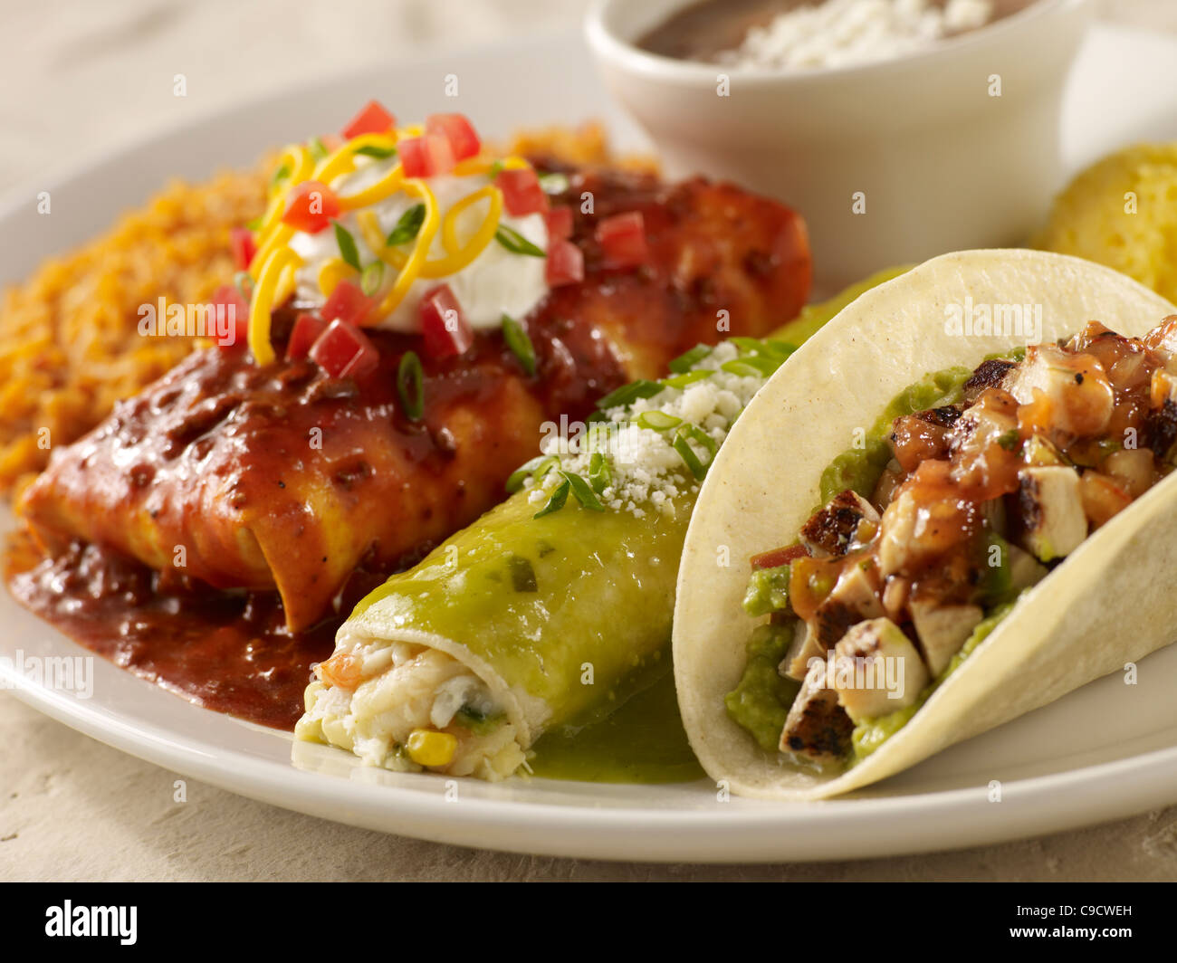 A chicken taco, burrito and seafood enchilada served with Spanish rice and black beans on a white plate Stock Photo