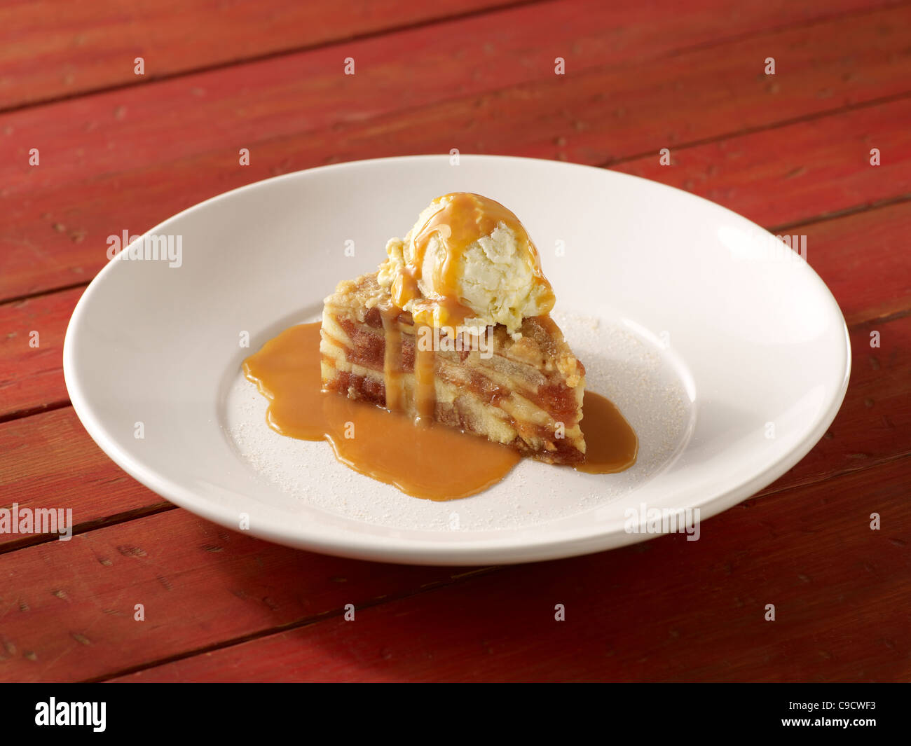 A slice of apple pie a la mode with caramel sauce on a white plate