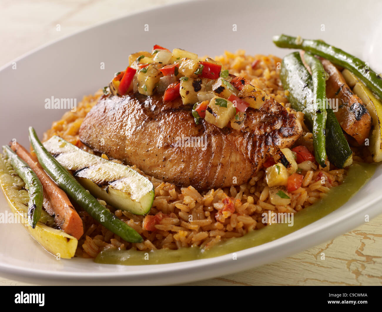 A salmon fillet topped with salsa and served over Spanish rice with grilled vegetables in a white bowl Stock Photo