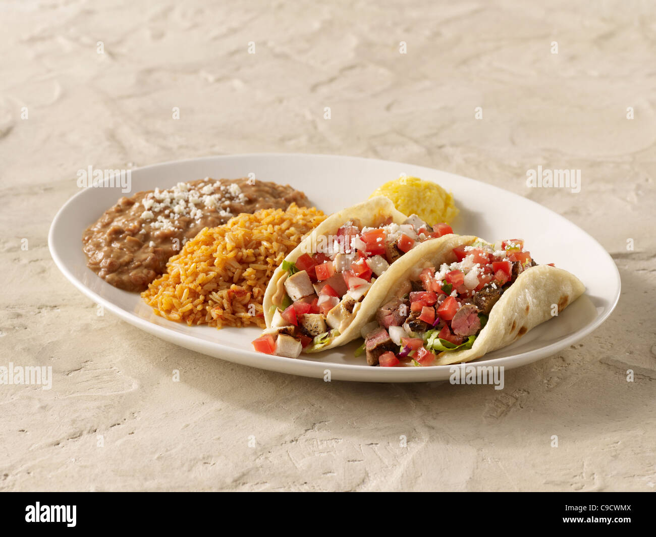 A fajita chicken taco and steak taco combo topped with salsa fresca and cheese and served with spanish rice and refried beans Stock Photo