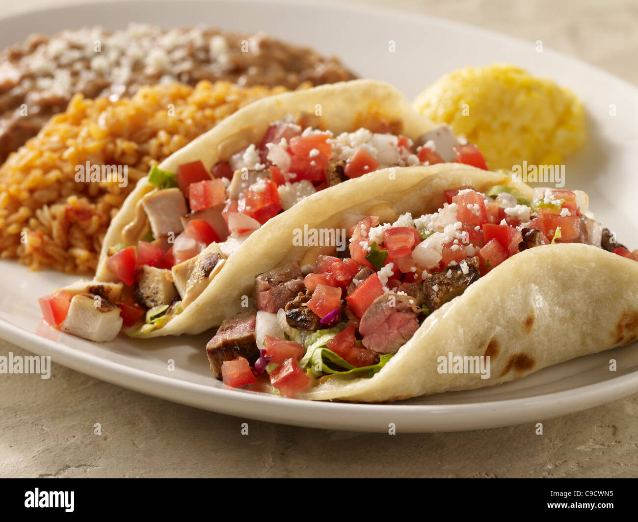 One steak and one chicken taco topped with salsa fresca and cheese served with refried beans and Spanish rice Stock Photo