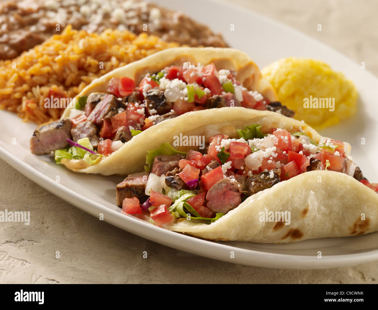 Two steak fajita tacos topped with salsa fresca and cheese and served with refried beans and Spanish rice Stock Photo