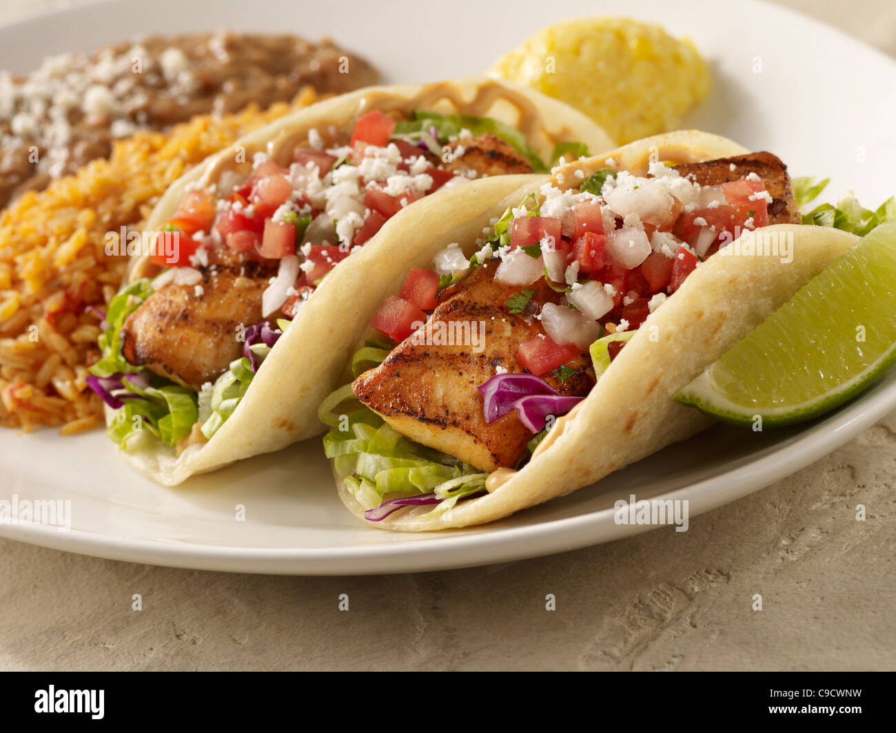 Two fresh fish taco topped with salsa fresca and cheese and served with refried beans and Spanish rice Stock Photo