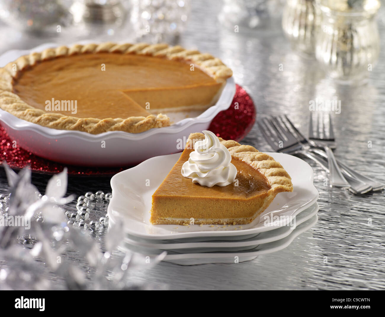 A pumpkin pie slice with a whole pie in the background in a holiday setting Stock Photo