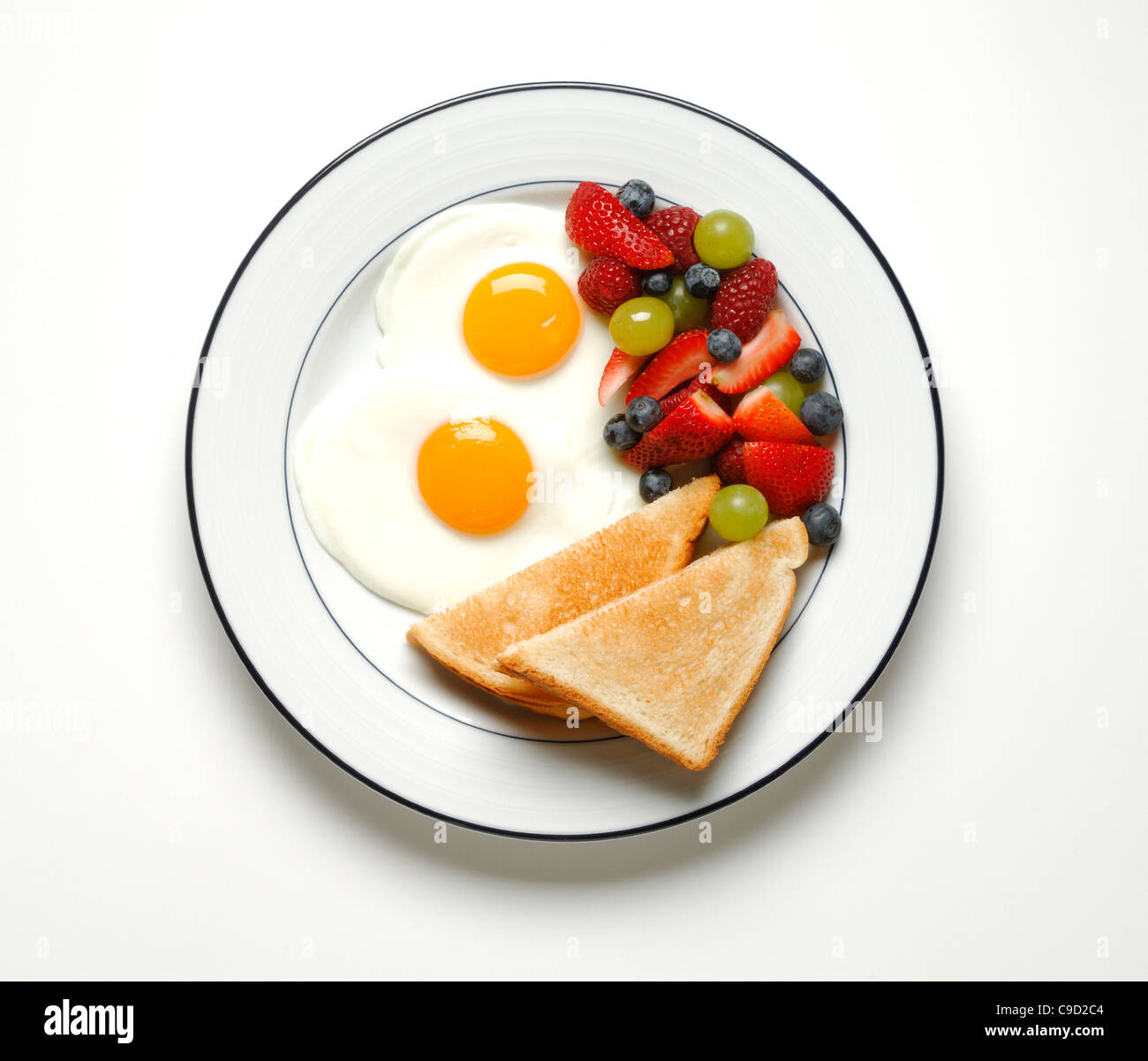 Two fried eggs, two slices of toast and fruit salad on plate Stock