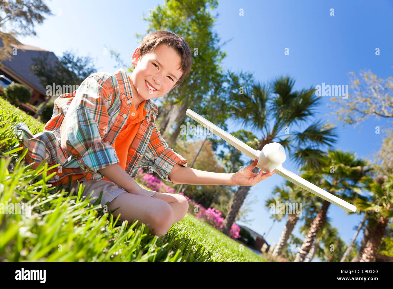 A young boy sitting on grass outside playing with a toy model airplane ...