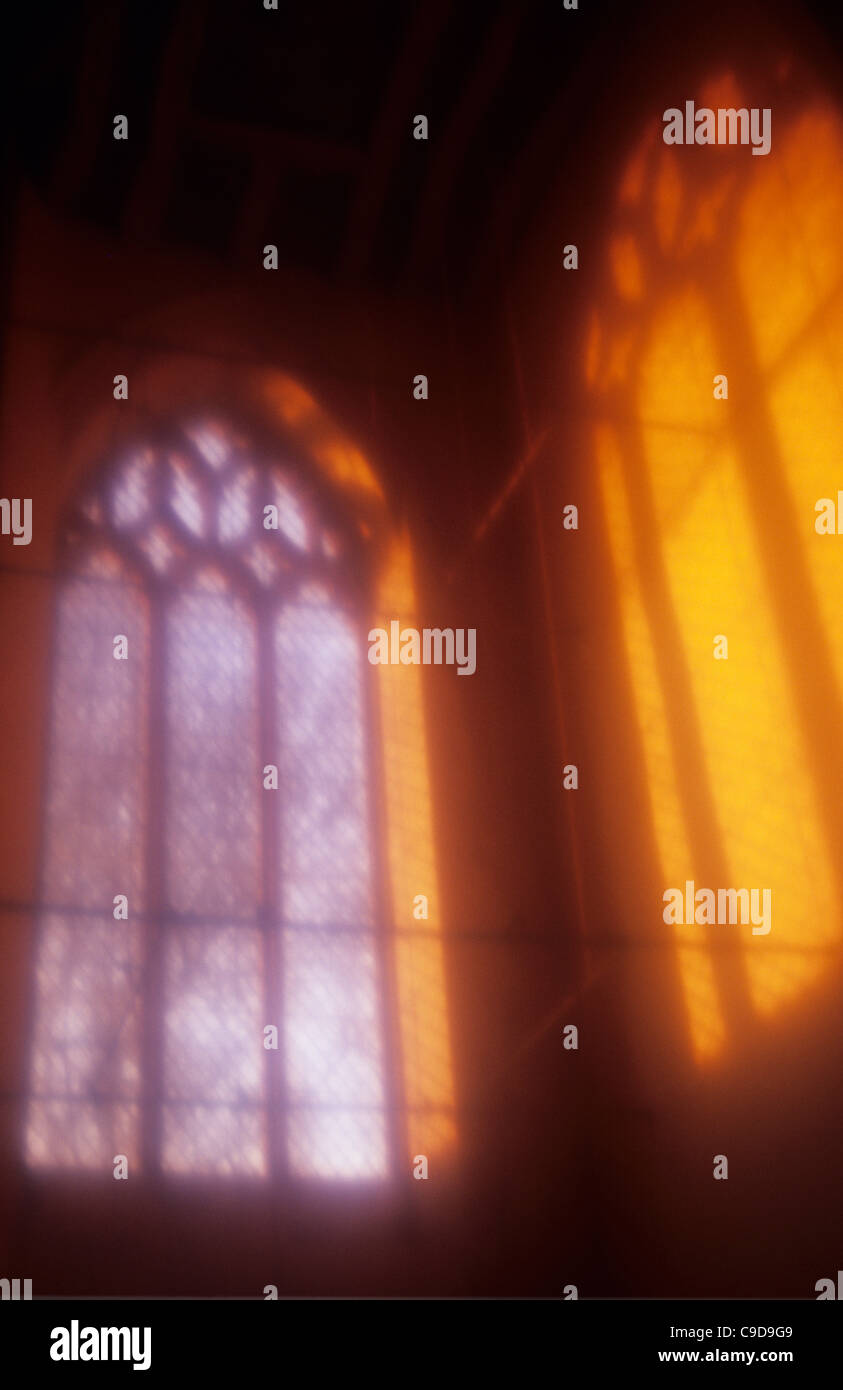 United Kingdom, Norfolk, Atmospheric view of diamond leaded church window next to projection onto wall of light from decorated Stock Photo