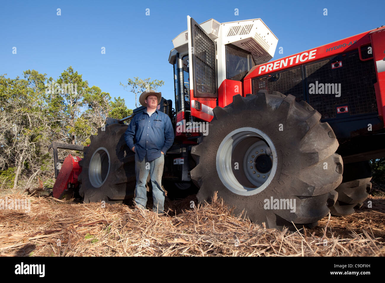 Contractor Chance Warden of Burnet, Texas stands next to a massive tractor that cuts cedar trees at Camp Bullis, San Antonio TX Stock Photo