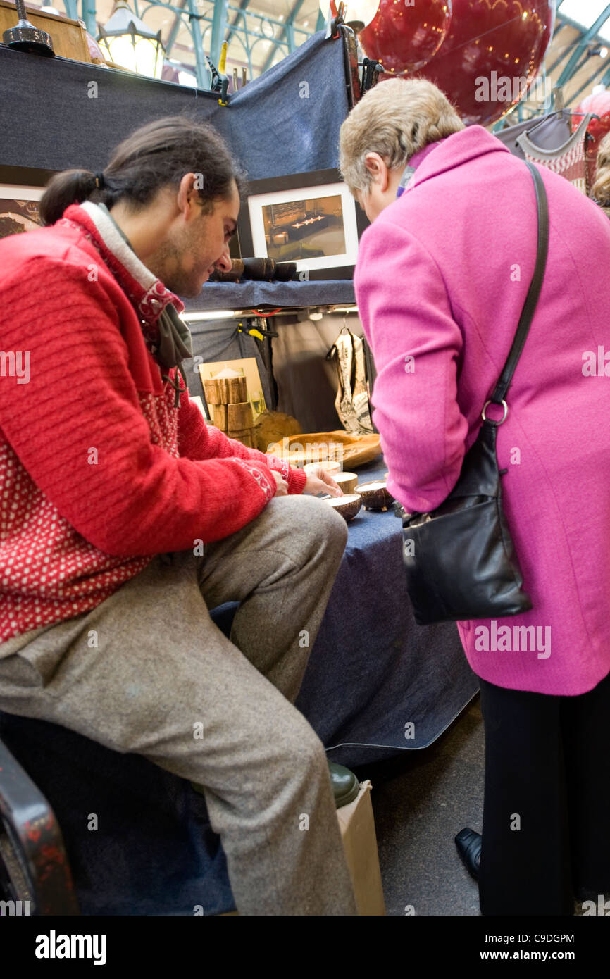 London Covent Garden Market stall holder young man ponytail elderly lady his wares wood wooden bowls Stock Photo