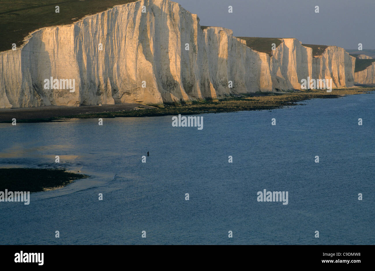 A lone fisherman stands in the cuckmere estuary under the cliffs of the Seven Sisters near Eastbounre, East Sussex, England. Stock Photo