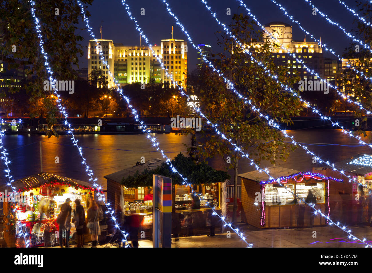 German Christmas Market Stalls on the South Bank, London at night, looking through lines of Xmas lights across to New Adelphi Stock Photo