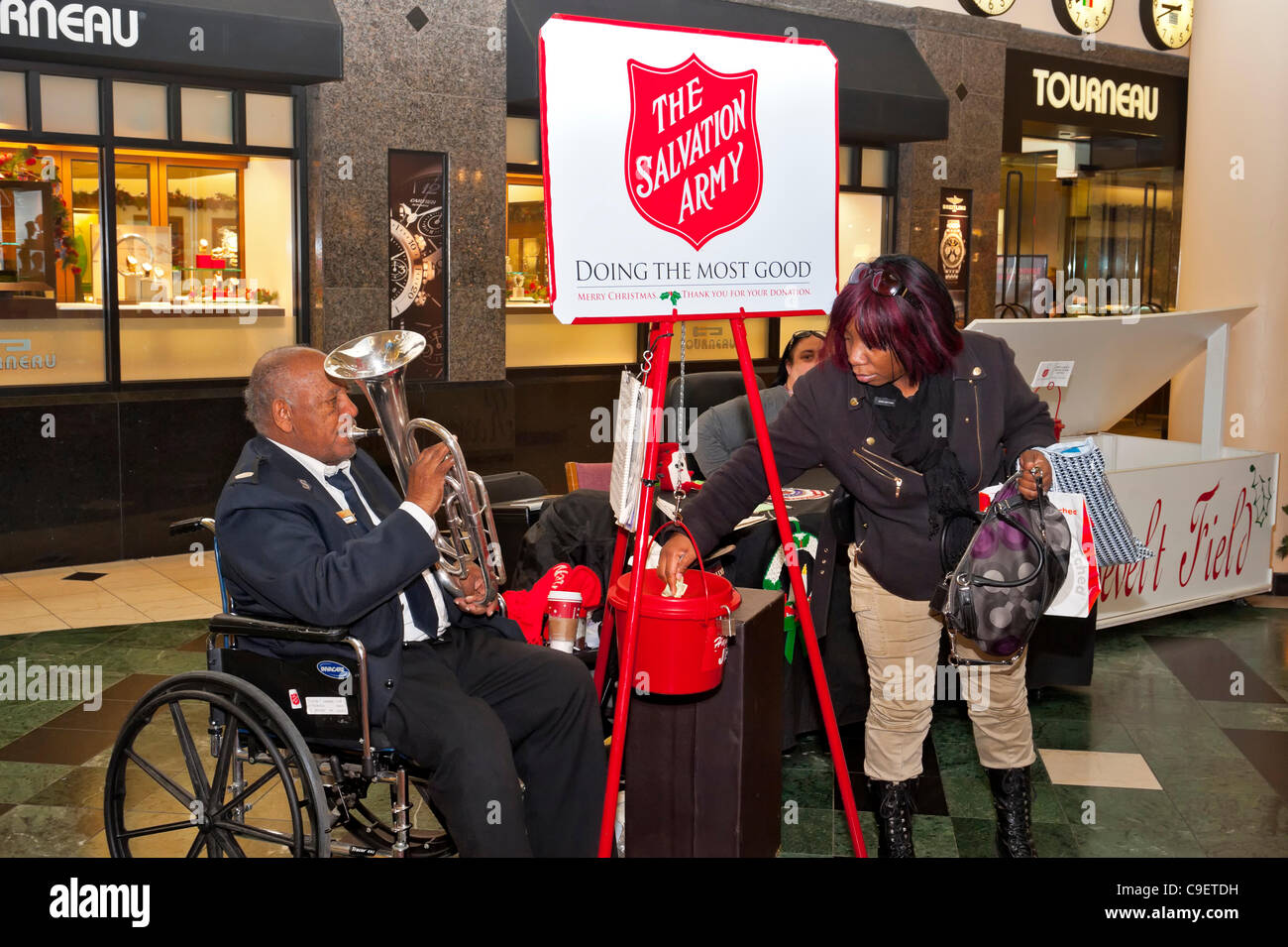 GARDEN CITY, NY, USA - DECEMBER 09: Shopper (right) donates money to Red Kettle Christmas Campaign of Hempstead's Salvation Army, a charitable and religious organization, at Roosevelt Field Shopping Mall, New York, on Friday, December 9, 2011. Musician NEVILLE LYTTLE, in wheelchair, played trumpet. Stock Photo