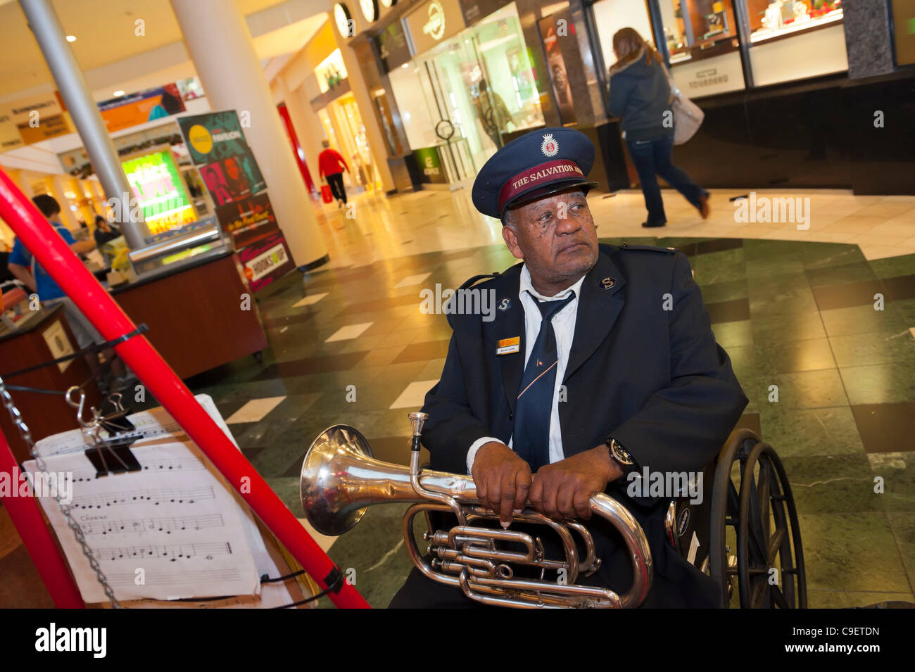 GARDEN CITY, NY, USA - DECEMBER 09: Salvation Army, a charitable and religious organization, member with trumpet helps raise funds for group's Red Kettle campaign at Roosevelt Field Shopping Mall, New York, on Friday, Dec. 9, 2011. Musician Neville Lyttle (in wheelchair) came from Hempstead group. Stock Photo