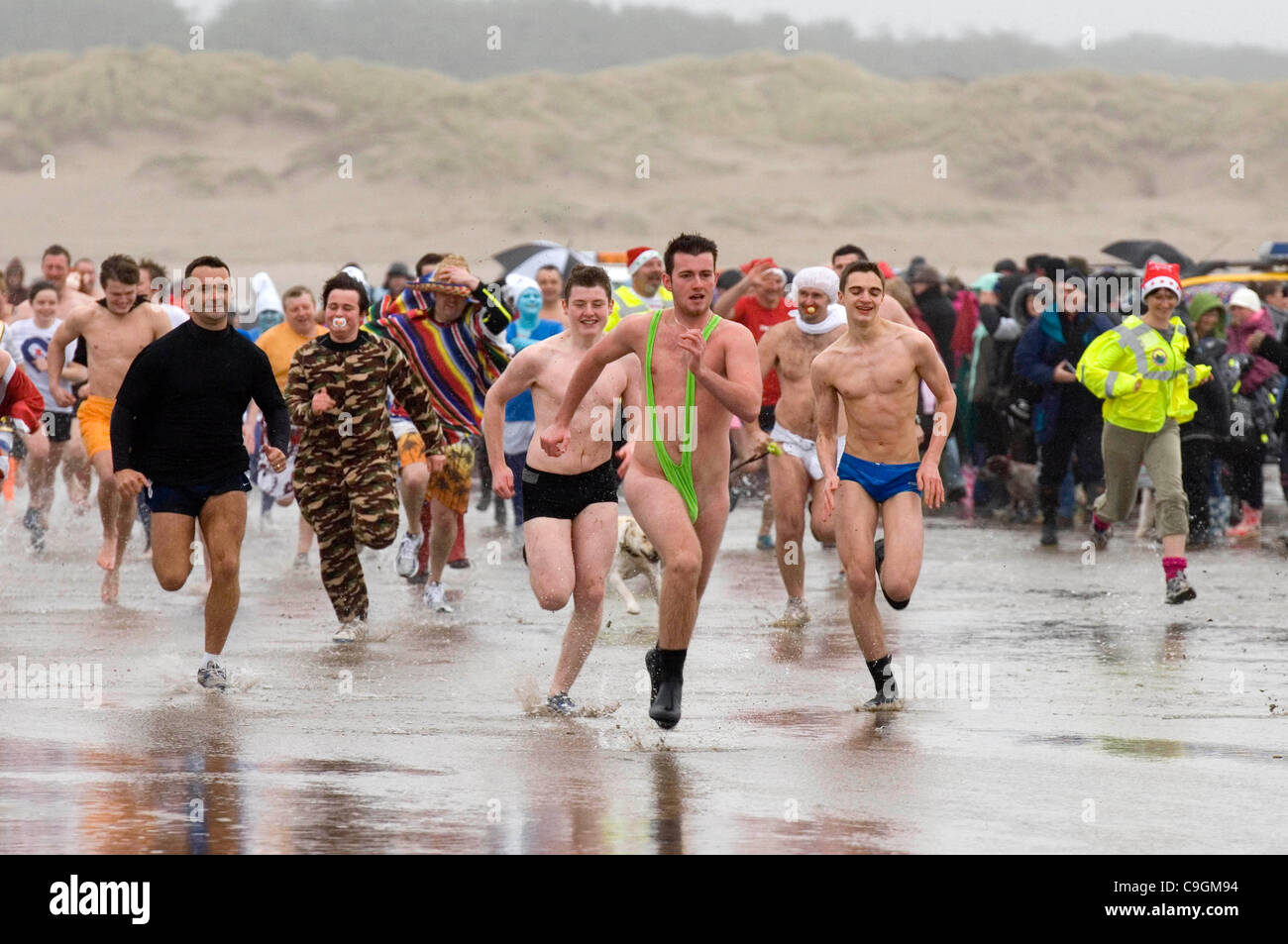 Pembrey, Llanelli, UK. 26th Dec, 2011. Swimmers racing into the sea at the annual Boxing Day 'Walrus Dip' at Cefn Sidn beach in Pembrey near Llanelli today. The leading runner at the front is wearing a mankini. Stock Photo