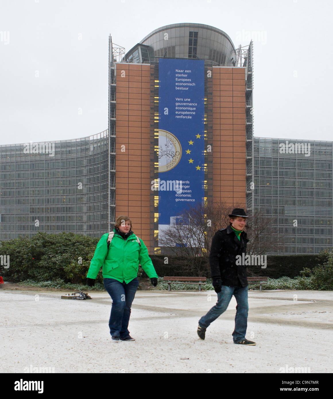People walk to work in the snow past the European Commission Berlaymont building in Brussels on the morning of the general strike called by the unions in Belgium. Stock Photo