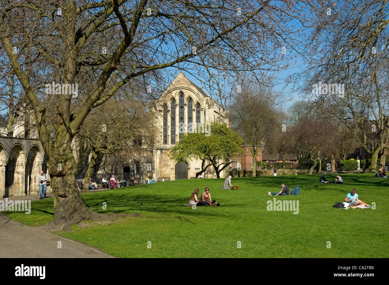 People visitors relaxing in Dean's Park and Minster Library in the background in spring York North Yorkshire England UK United Kingdom Great Britain Stock Photo