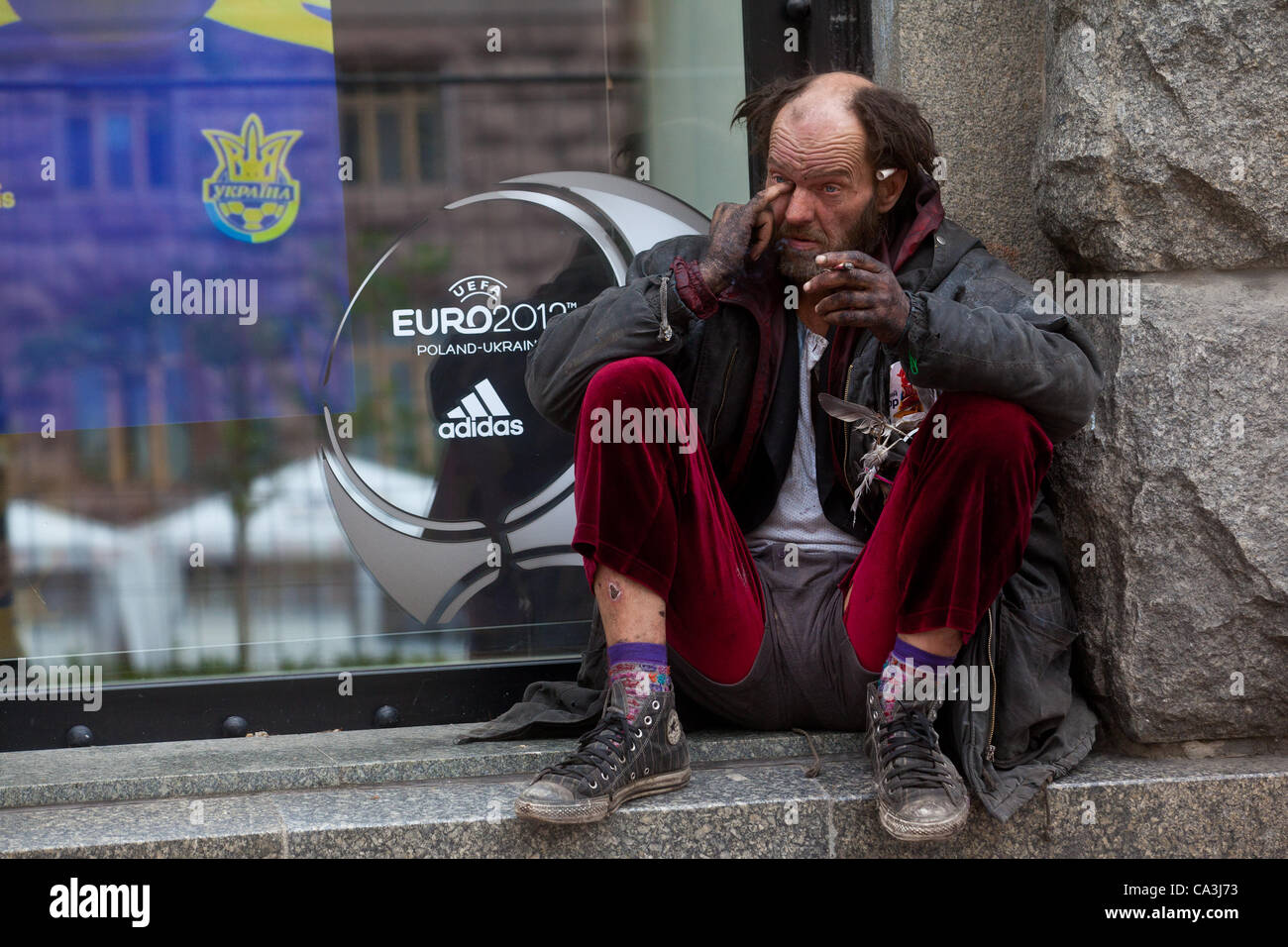 01.06.2012. Kiev, Ukraine. A homeless man sits near the front of shop windows logo EURO 2012, 1 June 2012. The Euro 2012 tournament in Poland and Ukraine runs from June 8 to July 1 Stock Photo