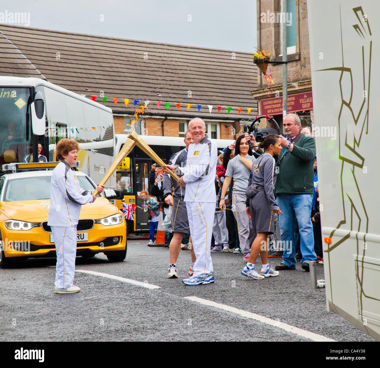 Friday 8th June 2012. North Ayrshire, Scotland, UK. Angela Oakley, 53, a Fairtrade campaigner from Glasgow passes the Olympic Flame to Thomas Tracey, 59, a charity marathon runner from Glasgow in Barrmill, North Ayrshire Stock Photo