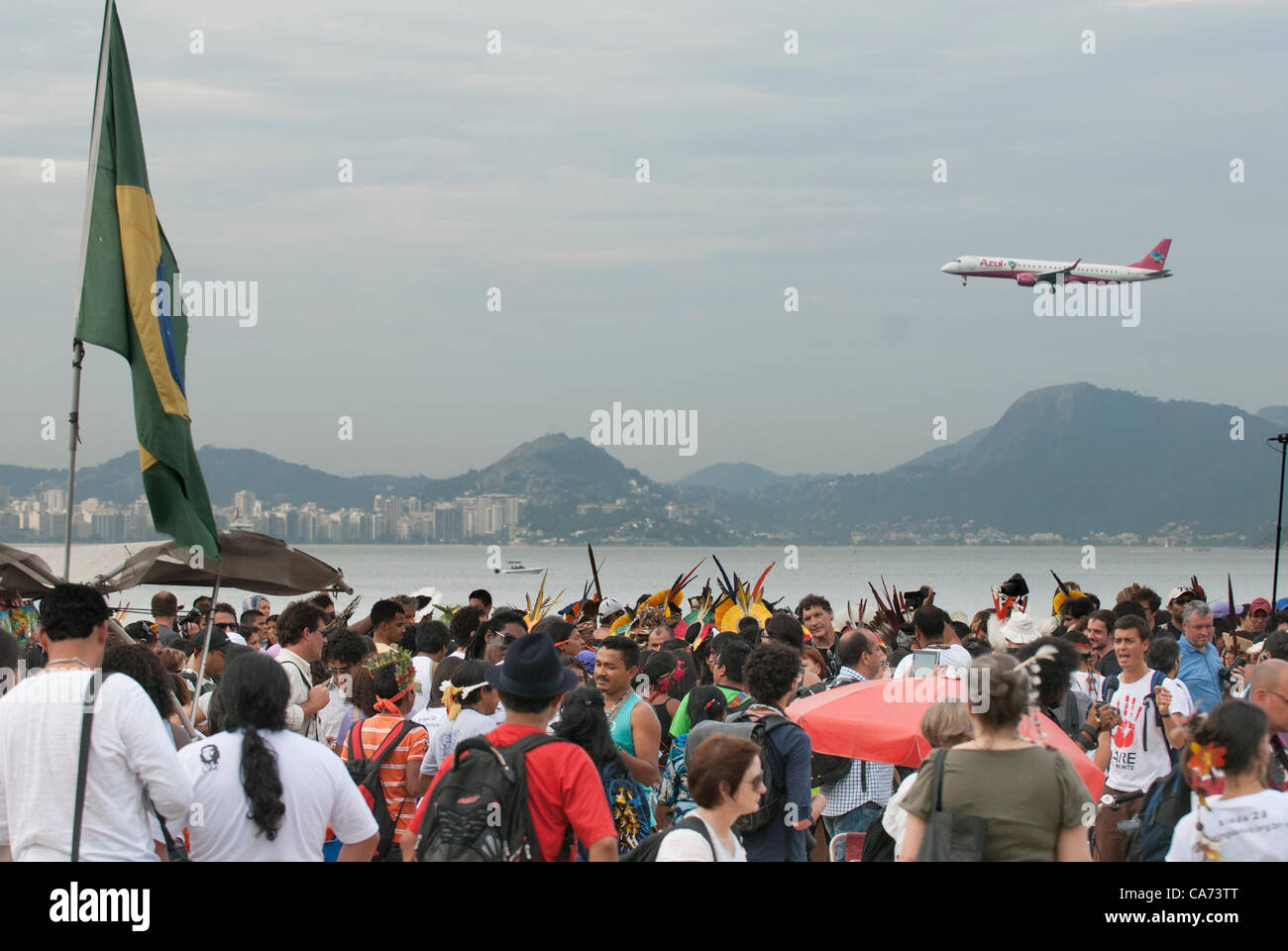 Indigenous people and others are gathering on Flamengo beach for the Human Banner event to protest about the construction of hydroelectric dams on Brazil's rivers while a jet aircraft flies over. The People's Summit at the United Nations Conference on Sustainable Development (Rio+20), Rio de Janeiro, Brazil, 19th June 2012. Photo © Sue Cunningham. Stock Photo