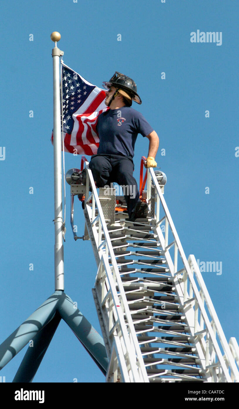 0956--Firefighter-paramedic Matt Alexander works from an extended ladder to attach a new flag onto the pole above Del Norte Place (apartments, restaurants and shops) at 11740 San Pablo Ave. Feb. 18, 2004 in El Cerrito, Calif.   Alexander is with El Cerrito fire department Engine 71.  The fire depart Stock Photo