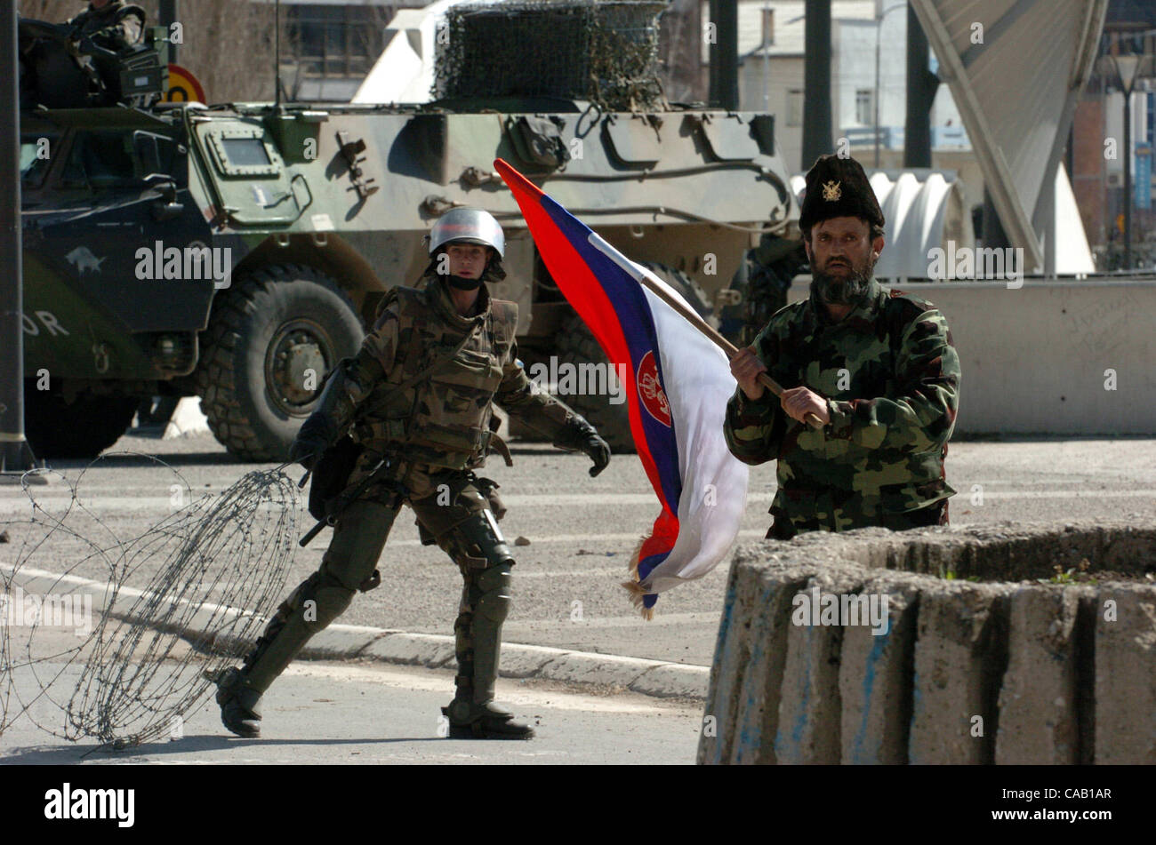 Mar 22, 2004; Kosovo, SERBIA; An unidentified Kosovo Serb civilian, dressed in camouflage uniform and traditional headgear, waves the Serbian flag in front of NATO-led peacekeepers armored vehicles in the northern Kosovo city of Kosovska Mitrovica. Several hundred Serbs have been evacuated from the  Stock Photo