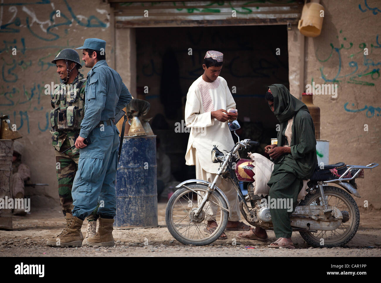 Afghan National Police Lt. Naib (second from left) interacts with an Afghan National Army soldier outside a fuel store in the Hazar Joft Bazaar while manning a vehicle checkpoint here, April 10, 2012. Stock Photo