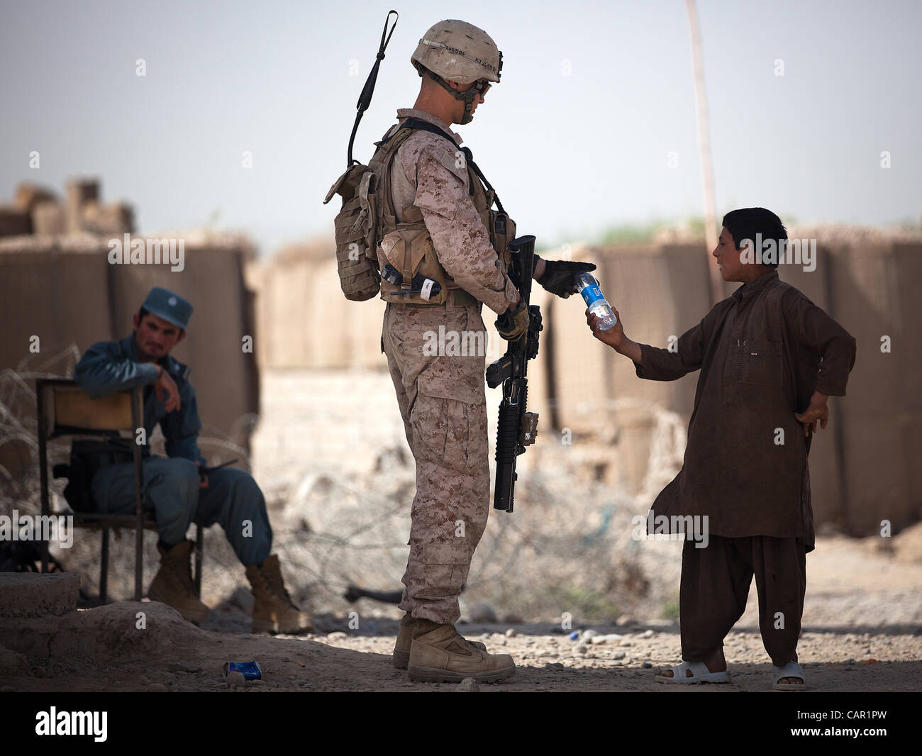 U.S. Marine Cpl. Mark Jensen, a team leader with 4th Platoon, Kilo Company, 3rd Battalion, 3rd Marine Regiment, and 22-year-old native of Nyssa, Ore., shares a water bottle with an Afghan boy while providing security at a vehicle checkpoint outside the Hazar Joft Bazaar April 10, 2012. Stock Photo