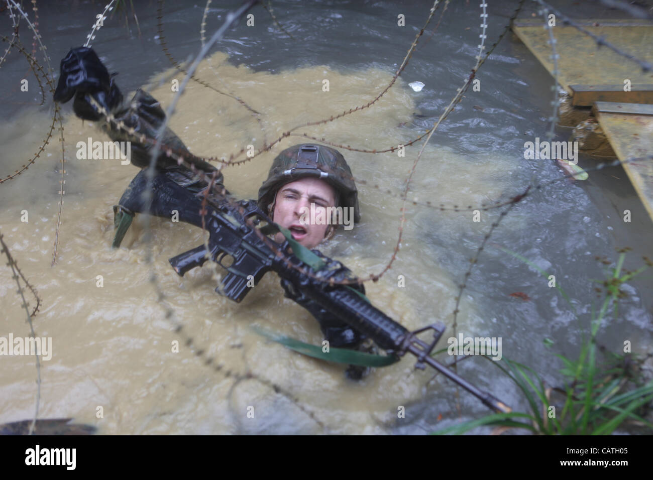 A US Marine crawls through a watery ditch and under concertina wire during the Jungle Endurance Course April 20, 2012 in Okinawa, Japan. Stock Photo