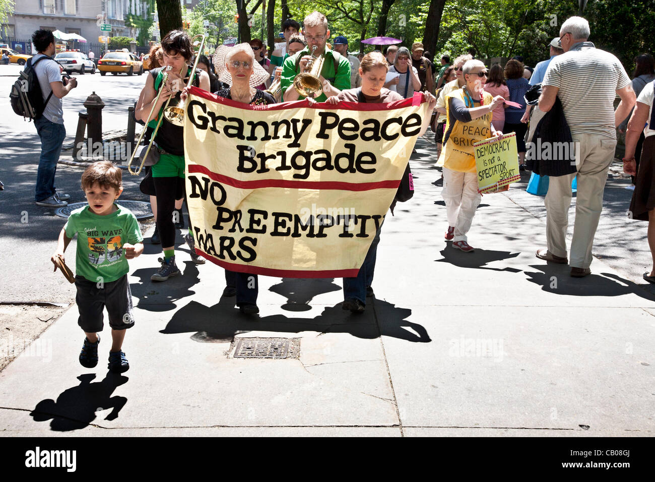 two women holding banner lead musicians & marchers along Fifth Avenue sidewalk on the Granny Peace Brigade sixth annual Mother's day Peace Stroll on a beautiful Mother's Day afternoon in New York City Stock Photo