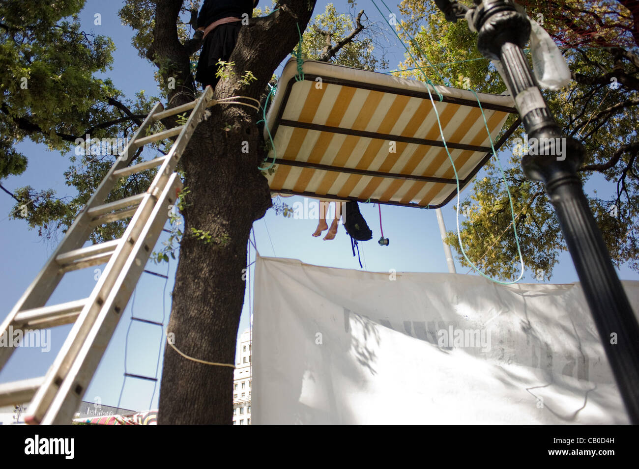 14 May, 2012-Barcelona, Spain.Feet are seen on a a bed hanging in a tree in the square.  After the demonstration of May 12, the movement of the Indignados (indignant) has returned at the Catalunya Square (center of Barcelona), birthplace of the movement  a year ago. Stock Photo