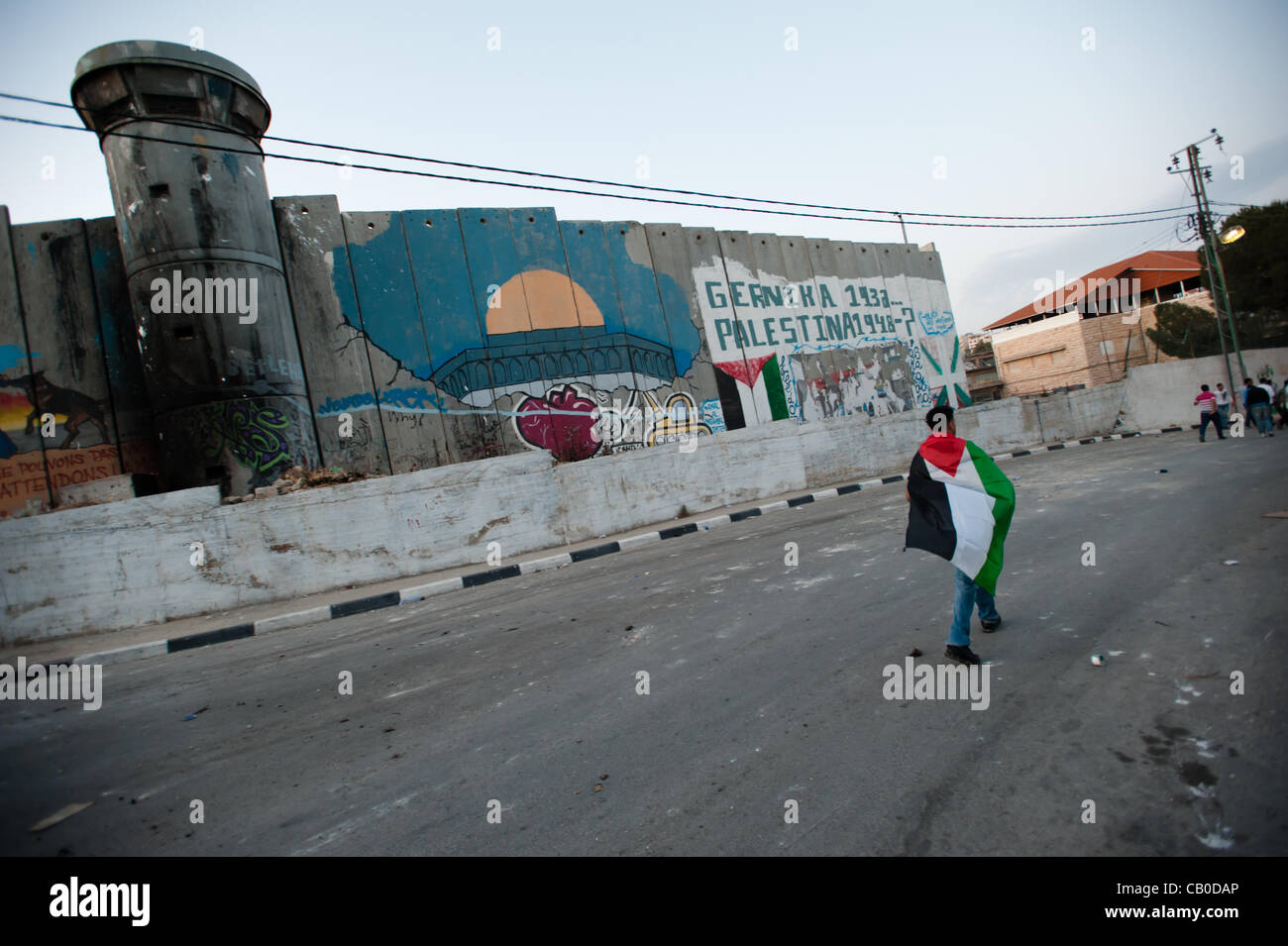 BETHLEHEM, PALESTINIAN TERRITORIES - MAY 14, 2012: A Palestinian wearing a flag marches past the Israeli separation wall in Aida Refugee Camp on the eve of Nakba Day, commemorating the "catastrophe" that expelled Palestinian refugees from what became the modern state of Israel in 1948. Stock Photo