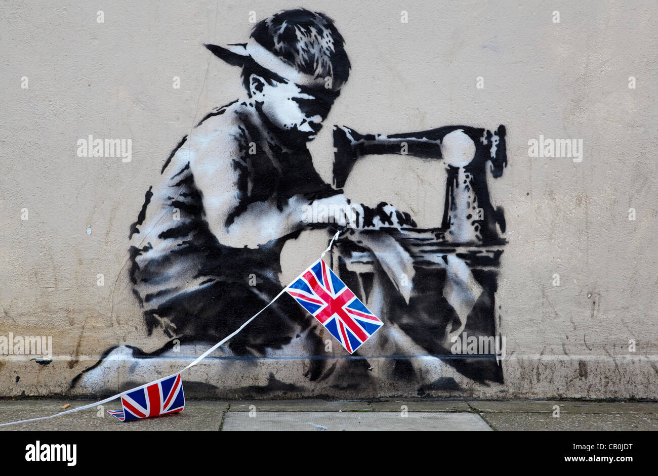 A new work from Graffiti Artist Banksy has appeared overnight in London. The piece depicts a Asian child stitching together Union Jack Bunting.  The work on the wall of retailer 'Poundland' is said to be Banksy's commentary on child labour and the upcoming Queen's Diamond Jubilee celebrations. Stock Photo