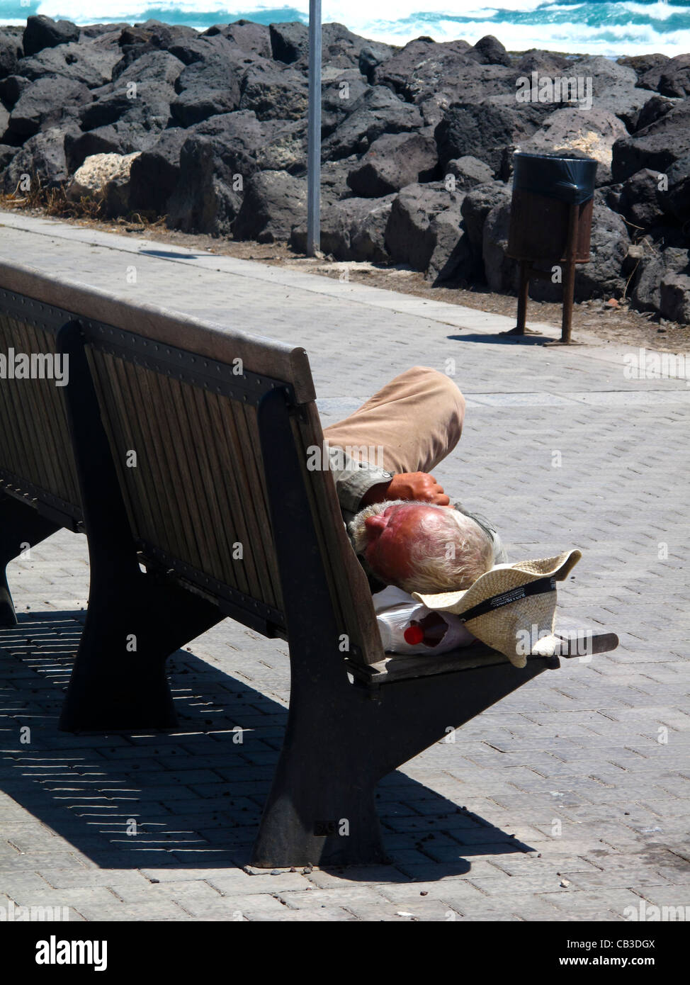 Tramp sleeping on wooden bench in sunshine Stock Photo