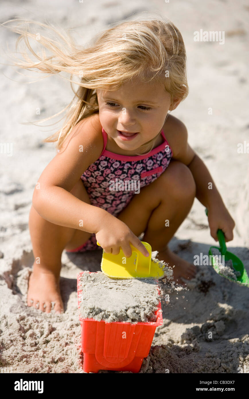 Girl playing with sand, beach buckets and shovel on beach Stock Photo