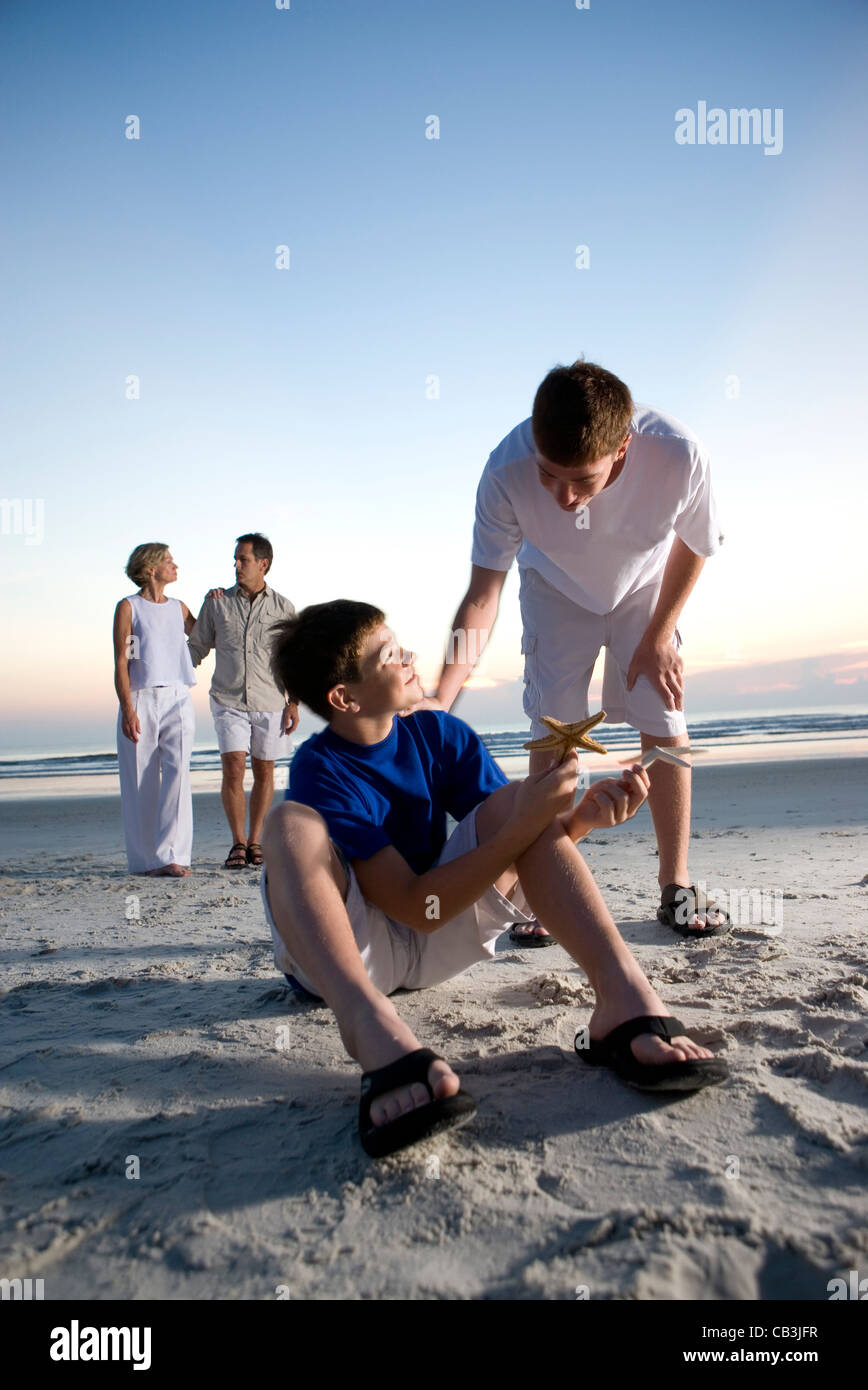 Boy showing starfish to his brother while parents stand on beach at sunrise Stock Photo