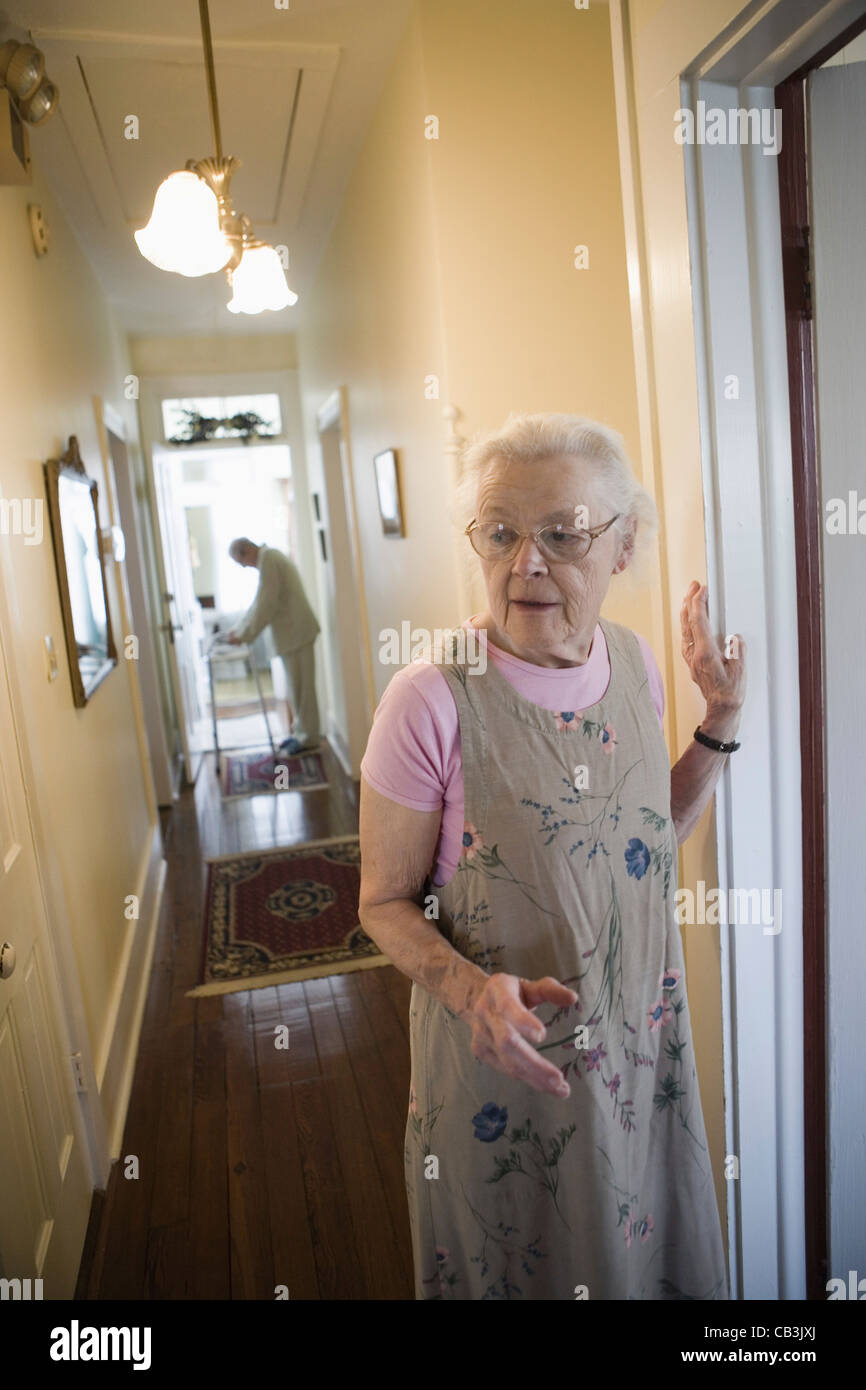 Elderly woman standing in hallway with feeble senior man in the background Stock Photo