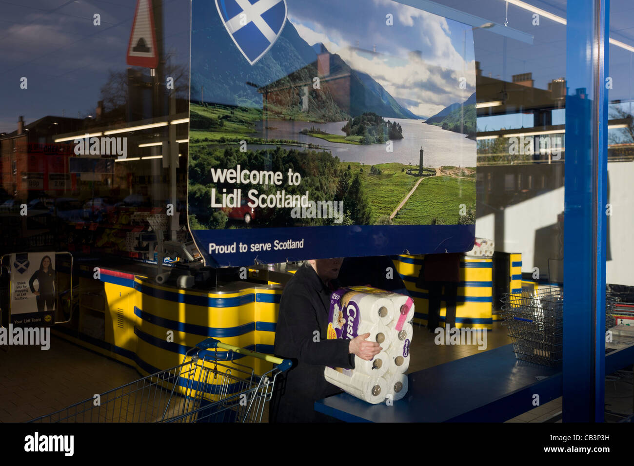 Shoppers inside Glasgow branch of supermarket Lidl with corporate colours and checkout counter & welcome to Scotland poster. Stock Photo