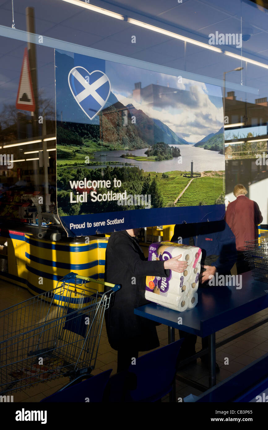 Shoppers inside Glasgow branch of supermarket Lidl with corporate colours and checkout counter & welcome to Scotland poster. Stock Photo