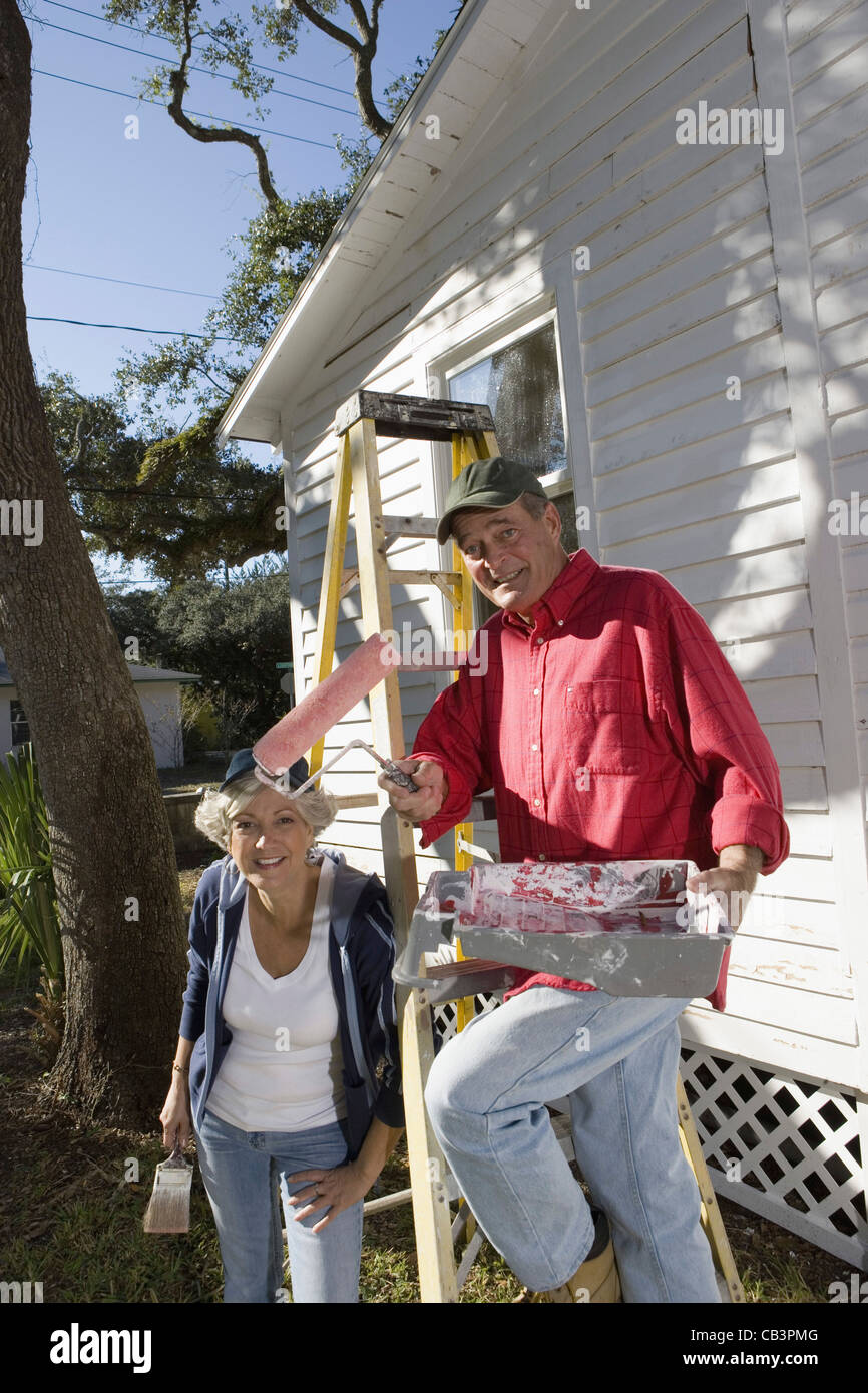 Mature couple with ladder and painting tools preparing to paint outside