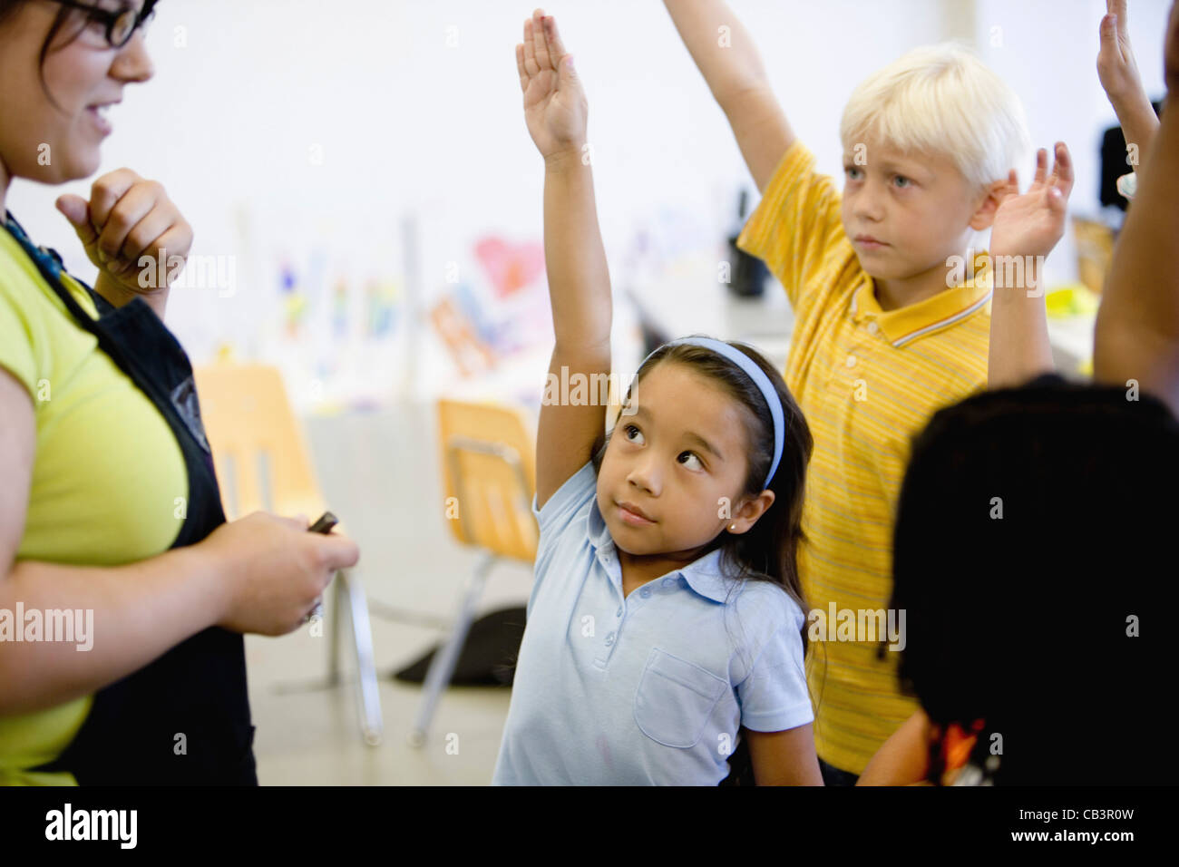 Teacher with her young students raising hands Stock Photo - Alamy