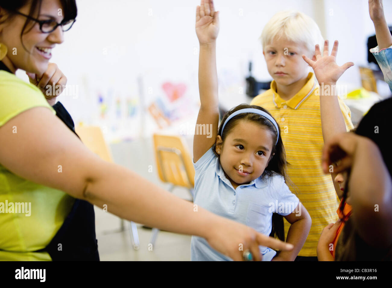 Teacher with her young students raising hands Stock Photo - Alamy
